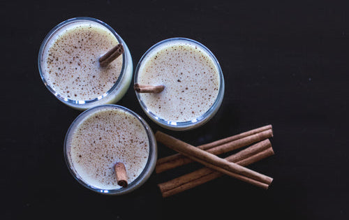 Three glasses of eggnog with a stack of cinnamon sticks