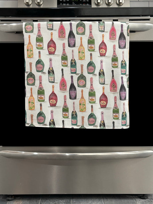 Kitchen Towel featuring a multicolor champagne bottle design. Pictured here hanging on a stove.