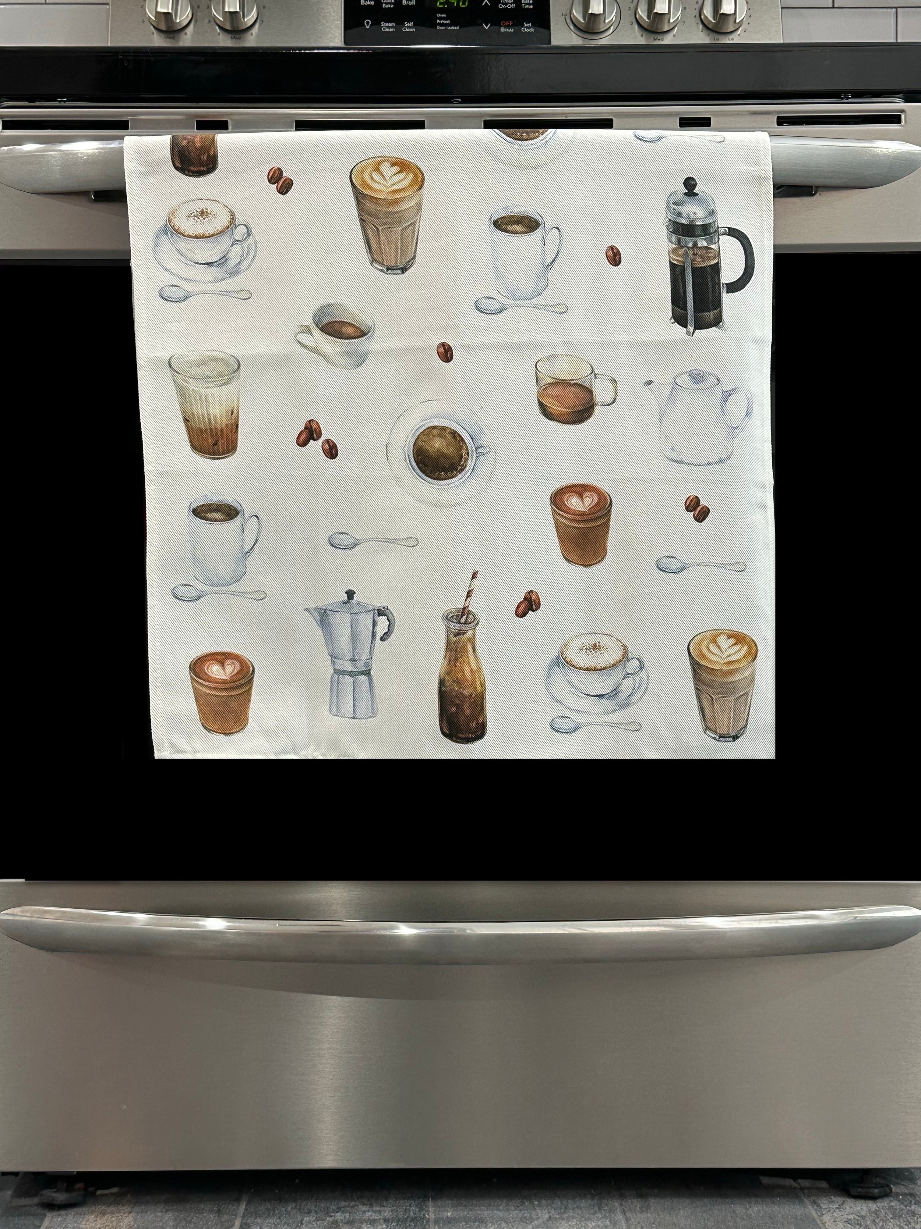 Kitchen Towel featuring a coffee design. Pictured here hanging on a stove.