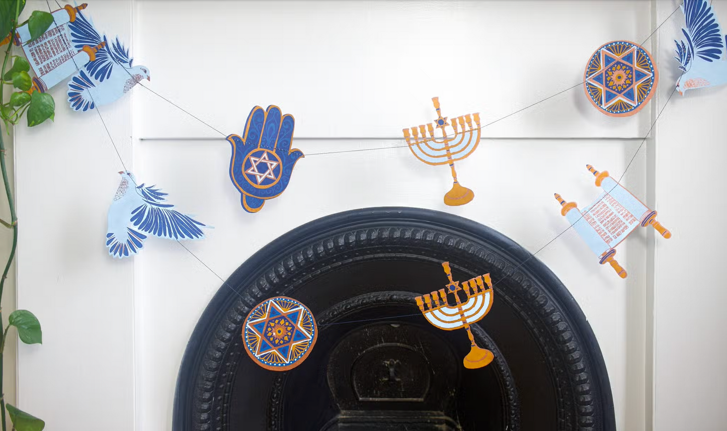 Hanukkah garland hanging above a fireplace. Includes symbols like a torah scrolls, menorahs, Star of David, dove birds, and the Hamsa.