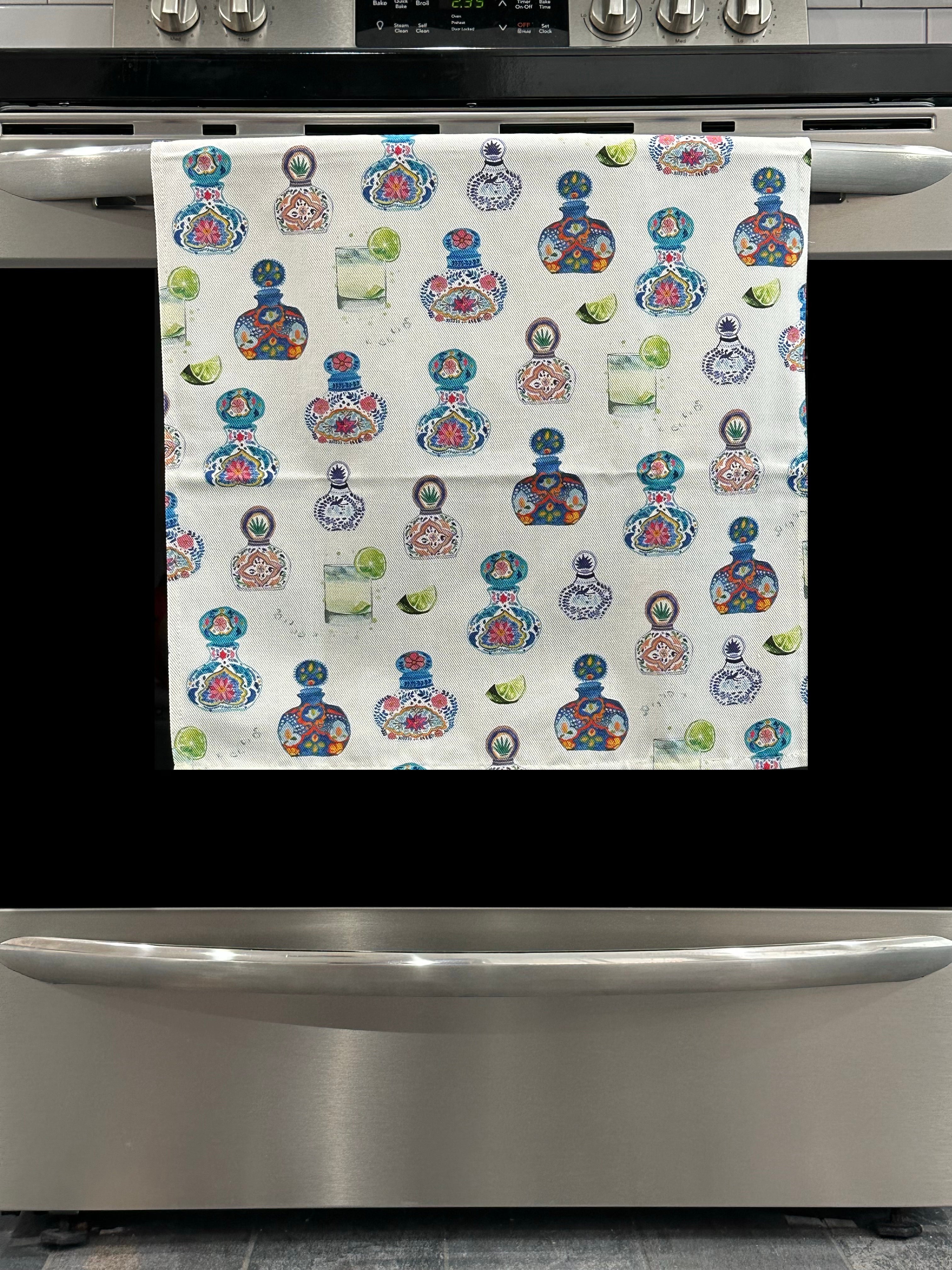Kitchen Towel featuring a multicolor tequila bottle and drink design. Pictured here hanging on a stove.
